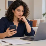 Mujer compara información en su celular y computadora antes de usar una app de préstamos.